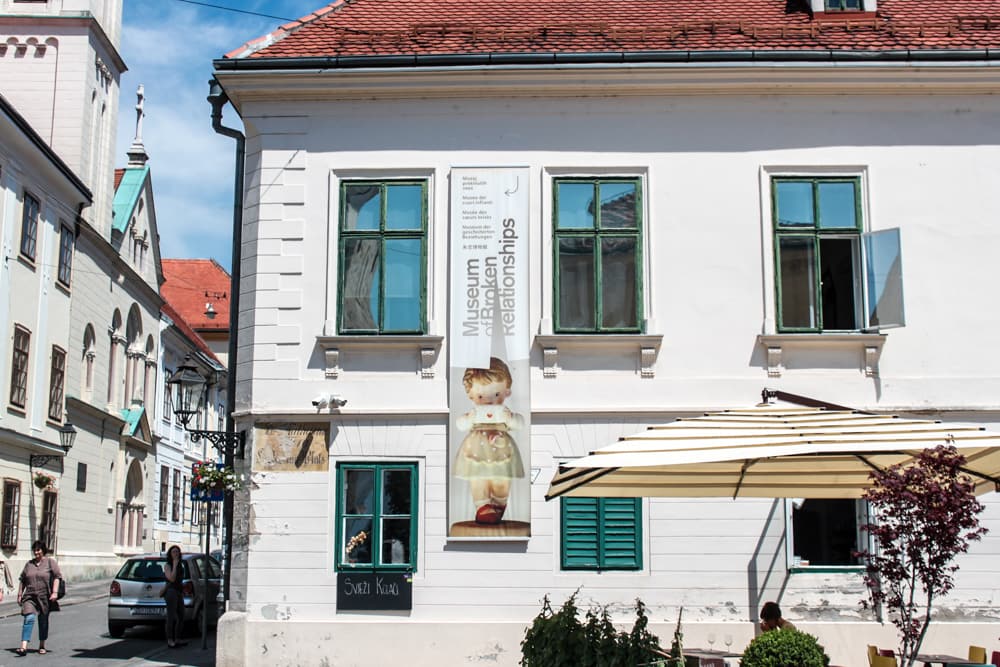 Fachada branca com janelas verdes do Museu das Relações Rompidas em Zagreb durante o dia.
