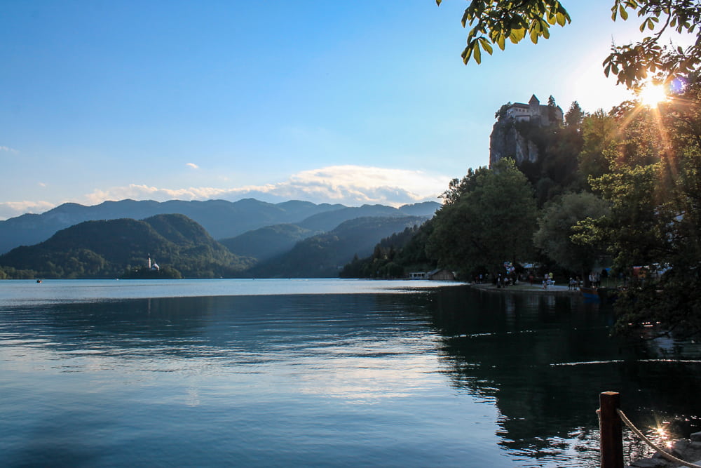 Roteiro Bálcãs: Pôr do Sol no Lago de Bled, com vista para o castelo no topo da montanha e Igreja da Assunção em uma ilha no meio do lago.