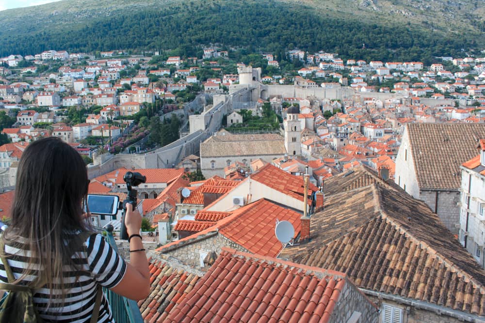 Roteiro Bálcãs: Vista da cidade medieval por cima da Muralha que a cerca e das muitas casinhas e árvores da cidade de Dubrovnik, com uma montanha ao fundo.