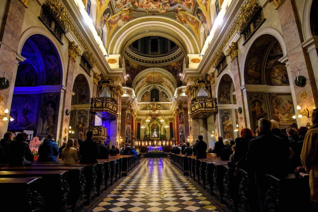 Catedral de Ljubljana vista do lado de dentro, iluminada e repleta de pinturas, mosaicos e detalhes em dourado. 