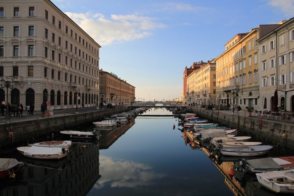 Canal de Trieste no fim da tarde. Ao centro canal com barcos ancorados e os prédios típicos italianos nas laterais