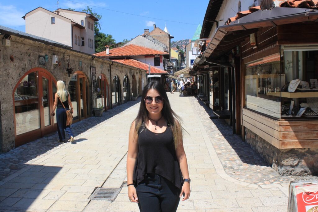 Marjorie vestida de preto e parada no meio de uma das ruas do grande mercado de Sarajevo