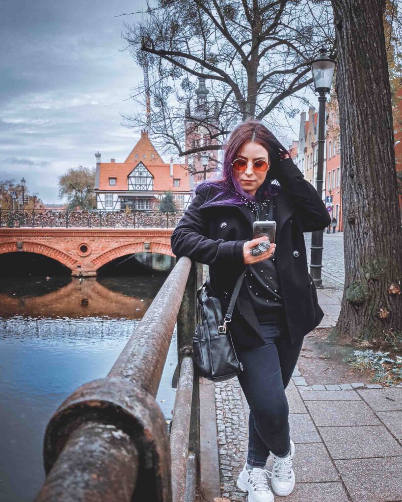 Usar internet no celular no exterior. Marjorie ao lado de um canal em Gdansk, com uma ponte e a Prefeitura da cidade ao fundo.