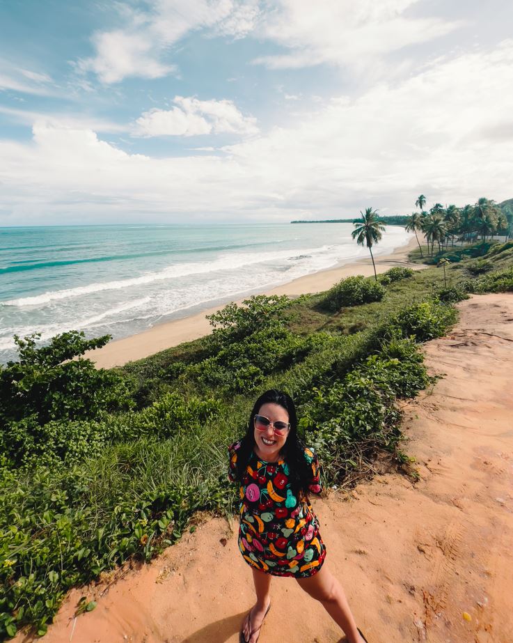 Marjorie no Mirante Barreira do Boqueirão, que é cercado pela vegetação nativa e tem vista para o mar e os coqueiros margeando a praia.