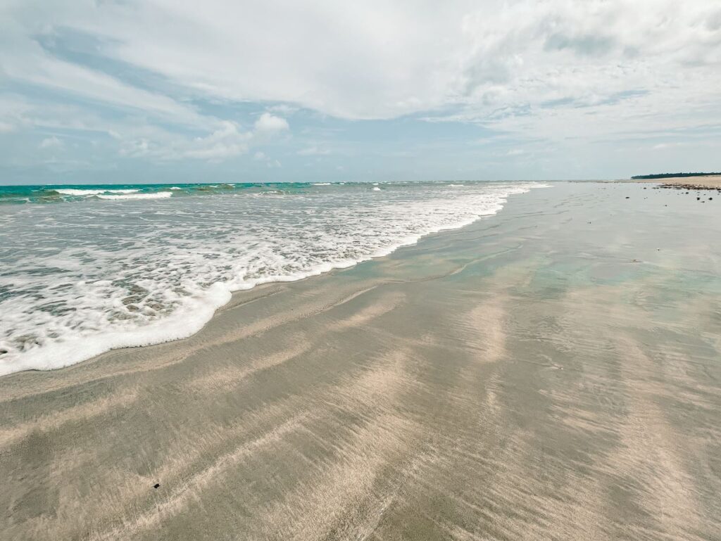 Grande extensão de areia da deserta Praia de Pontal do Boqueirão, com o mar de poucas ondas e maré baixa.