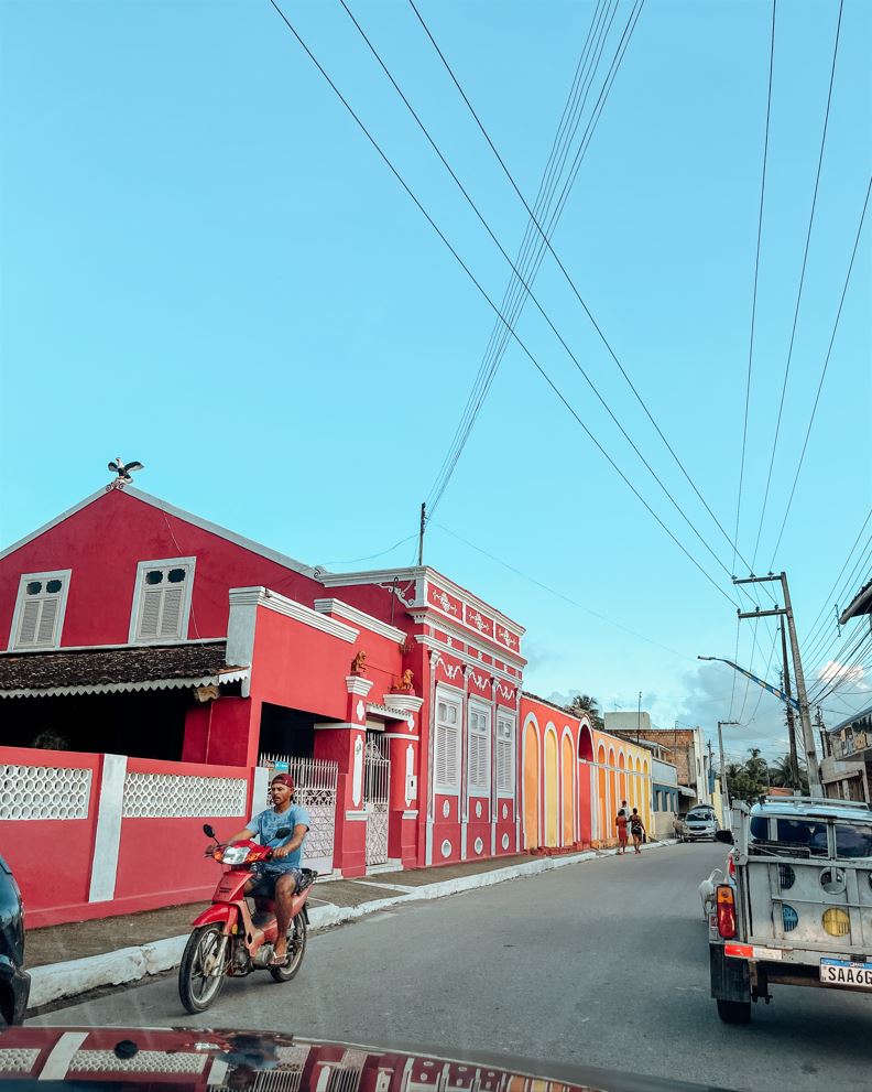 Carro passando em uma rua com casinhas coloridas no centro de Passo de Camaragibe.